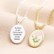Back of Meaningful Word Enamel Flower Pendant Necklace in Silver next to front of gold version on neutral coloured material