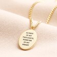 Back of Meaningful Word Enamel Flower Pendant Necklace in Gold on top of beige fabric