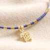 Close up of charm on Blue Miyuki Bead Turtle Charm Cord Anklet in Gold against beige fabric
