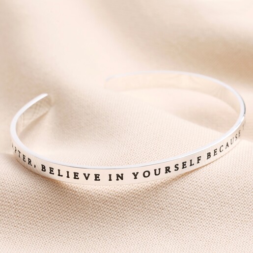 A New Chapter Meaningful Word Bangle in Silver on top of beige material