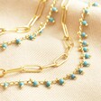 Close up of details on Teal Stone Droplet and Cable Chain Layered Necklace in Gold against beige fabric