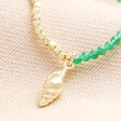 Close Up of Green Stone Beaded Shell Pendant Necklace in Gold on Beige Fabric