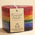 The Recycled Candle Company Heart Rainbow Pride Candle with label hanging from wick against neutral backdrop