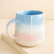 Sass & Belle Pastel Blue and Pink Ombre Mug on top of raised beige surface