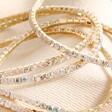 Close up of Set of 5 Clear Crystal Tennis Bracelets in Gold against neutral coloured fabric