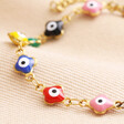 Close up of charms on Gold Stainless Steel Colourful Enamel Evil Eye Charm Bracelet against neutral fabric