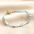 Evil Eye Blue and Green Seed Bead Bracelet in Gold on Beige Fabric