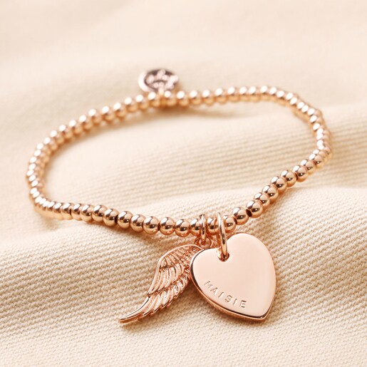 Personalised Beaded Wing Charm Bracelet in rose gold on top of neutral coloured material