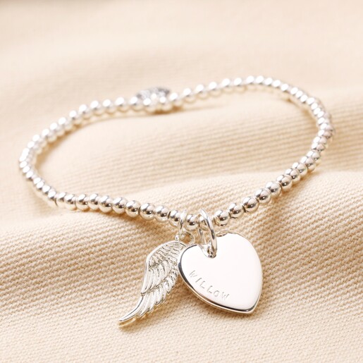 Personalised Beaded Wing Charm Bracelet in silver on top of beige coloured material