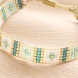 Close Up of Blue Beaded Woven Cord Bracelet in Gold on Beige Fabric