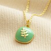 Green Enamel Organic Leaf Pendant Necklace in Gold on Beige Fabric