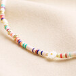 Close up of beads on Multicoloured Heishi and Daisy Charm Beaded Necklace in Gold against beige fabric