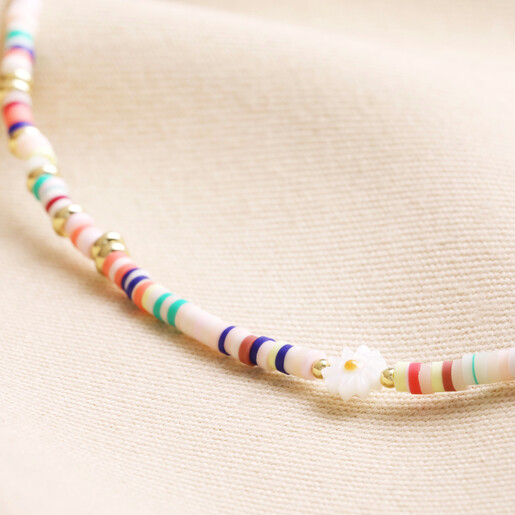 Close Up  Close up of beads on Multicoloured Heishi and Daisy Charm Beaded Necklace in Gold against beige fabric