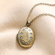 Close up of pendant from Personalised Photo Antiqued Crystal Star Oval Locket Necklace on top of beige fabric