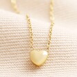 Close up of charm on Gold Stainless Steel Tiny Round Heart Charm Necklace against neutral backdrop