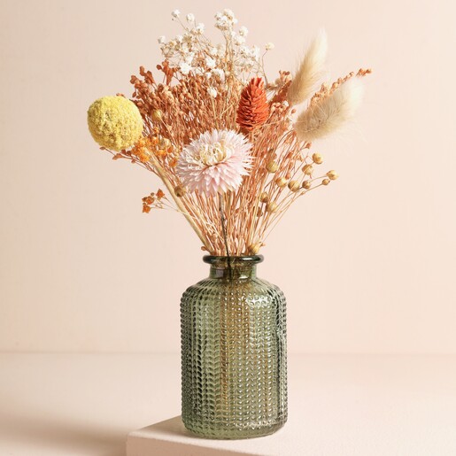 Green Glass Dimpled Bottle Vase with a spring-coloured posy on a beige background