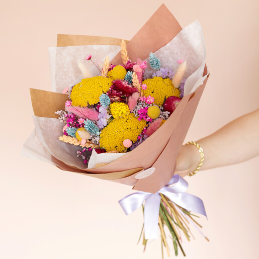 Model holding Luxury Rainbow Brights Dried Flower Bouquet against pink backdrop
