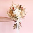 Model holding Nancy Dried Flower Bridal Wedding Bouquet against beige coloured backdrop