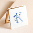 K Floral Initial Compact Mirror standing on top of neutral coloured backdrop