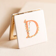 D Floral Initial Floral Initial Compact Mirror standing open on top of beige coloured backdrop