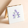 A Floral Initial Compact Mirror standing on top of neutral coloured backdrop