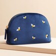 Small Navy Velvet Bee Wash Bag on top of raised surface against beige backdrop