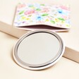 Pink Floral Round Compact Mirror and Pouch on Beige Surface Showing Mirror 