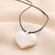 Close up of Chunky Heart Locket Cord Necklace in Silver on top of beige coloured fabric