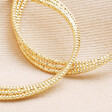 Close up of details on Triple Layered Thread Hoop Earrings in Gold against beige fabric