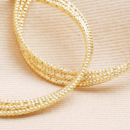 Close up of details on Triple Layered Thread Hoop Earrings in Gold against beige fabric