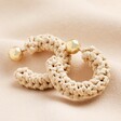 Beige Woven Hoop Earrings with Ball Backs against a beige material background