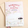 A Pale Pink Hardback Book With a Bathtub Illustration on a Neutral Background