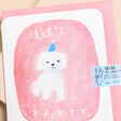 Close up of Laura Skilbeck Let's Party Dog Birthday Card with a white dog, blue party hat and pink background with pink card