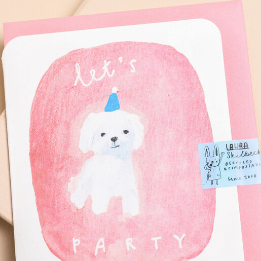 Close up of Laura Skilbeck Let's Party Dog Birthday Card with a white dog, blue party hat and pink background with pink card