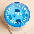 North Muse Crystal Cove Sea Salt & Sage Candle with blue lid on a neutral background