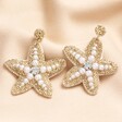 Bead and Pearl Starfish Drop Earrings in Gold against beige material background 