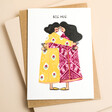 This card features two colourfully dressed women with wavy black hair wrapped in an embrace with their foreheads pressed together.