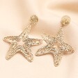 Oversized Hammered Starfish Outline Drop Earrings in Gold on neutral background