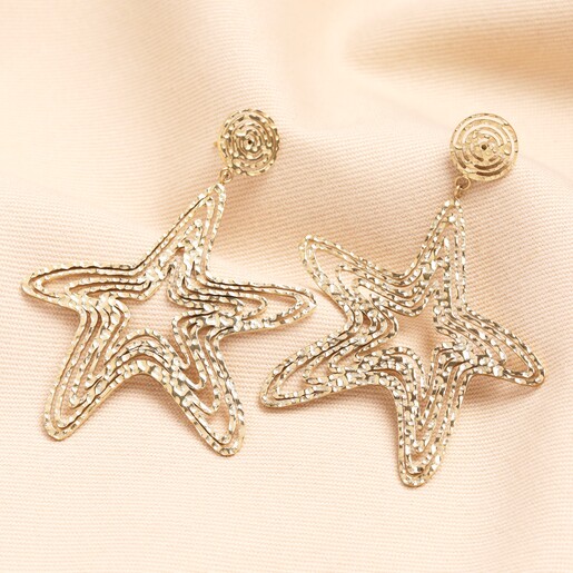 Close up Oversized Hammered Starfish Outline Drop Earrings in Gold on neutral background