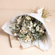 Mabel Bridal Bouquet with a selection of light coloured dried flowers wrapped in white paper on it's side against a neutral background