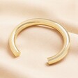 An oversized wide-band bangle in gold.