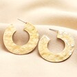 Oversized Hammered Flat Hoop Earrings in Gold on neutral background