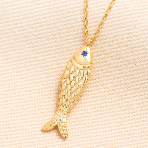 A Flat Gold Fish Pendant With a Sparkling Blue Crystal Eye