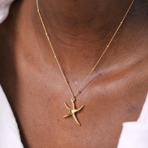 starfish pendant in gold against a pale pink background