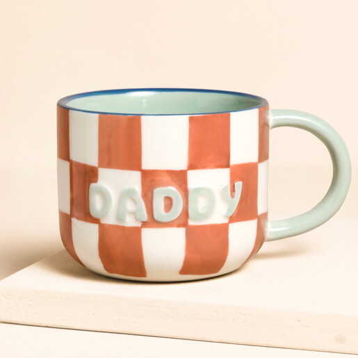 A Cream and Orange Checkerboard Print Ceramic Mug with a Green Handle and Daddy Wording