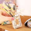 A Small Ceramic Vase in Cream with Gold Wording and Floral Cover Shaped Like a Book Filled with Dried Flowers
