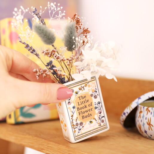A Small Ceramic Vase in Cream with Gold Wording and Floral Cover Shaped Like a Book Filled with Dried Flowers