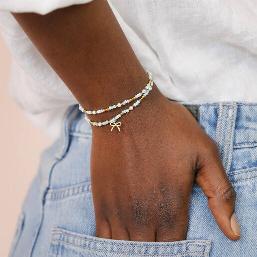 A Wrap Around Elasticated Bracelet with Green and Gold Beads and Pearl Accents Complete with a Dangling Gold Bow Charm