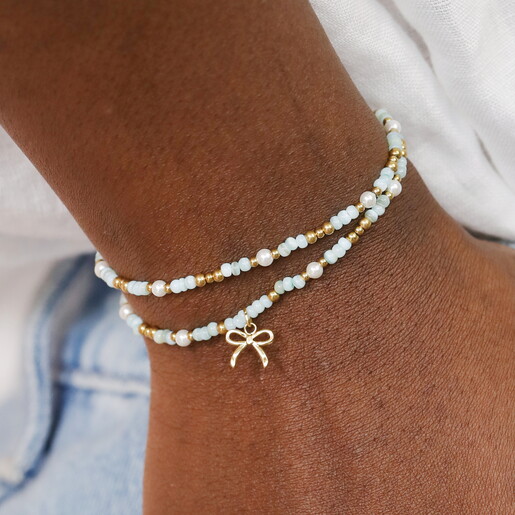 A Wrap Around Elasticated Bracelet with Green and Gold Beads and Pearl Accents Complete with a Dangling Gold Bow Charm