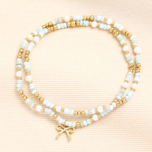 A Wrap Around Elasticated Bracelet with Green and Gold Beads and Pearl Accents Complete with a Dangling Gold Bow Charm